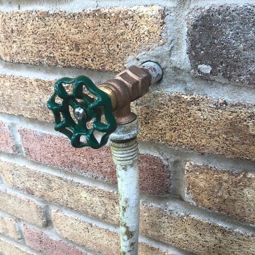 An outdoor garden hose being attached to a spigot outside a home in Bucks County, PA during spring.